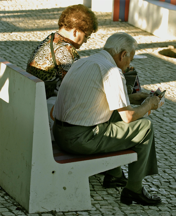 An elderly man and woman are shown sitting on a bench.