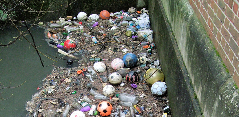 A photo of garbage that is washed up against a concrete wall.