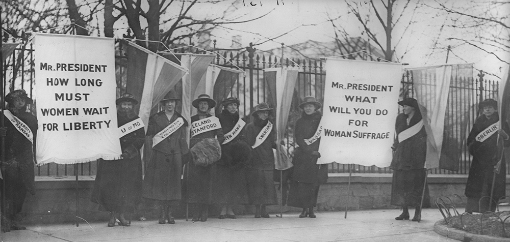 Figure (a) shows women’s suffrage marchers.