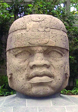 A photograph shows a massive carved stone head with a flat nose, large lips, and slightly crossed eyes.