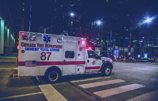 An image of a truck with flashing lights driving through an intersection. The side of the truck reads “Chicago Fire Department Emergency Medical Services”.