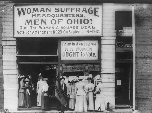 This photo shows several women outside of the Woman Suffrage Headquarters. A large sign reads “Woman Suffrage Headquarters. Men of Ohio! Give the Women a Square Deal. Vote for Amendment No. 23 on September 3, 1912.” A second sign reads, “Come in and learn why women ought to vote.”