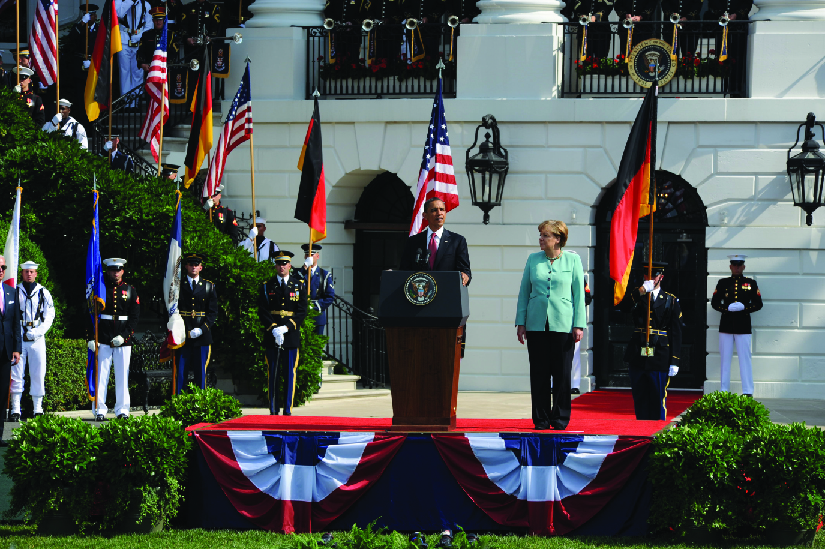 A photo of Barack Obama speaking outside the White House. Standing next to him is Angela Merkel.