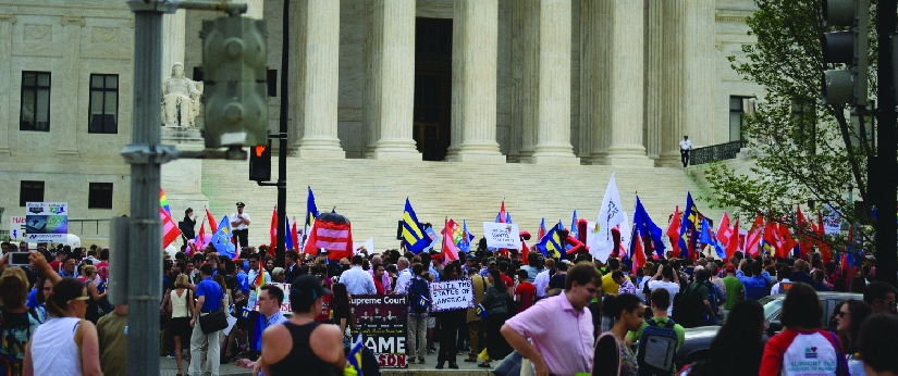 An image of a group of people standing in front of a building. Some people are holding signs.