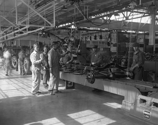 An image of a few people standing in an automotive plant next to some machinery.