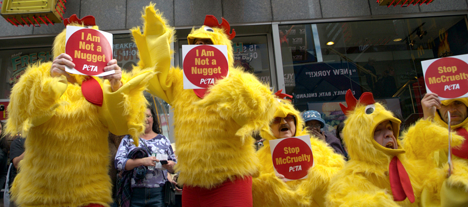Protesters are shown here wearing yellow chicken costumers and holding PETA signs that say “I Am Not a Nugget” and “Stop McCruelty.”