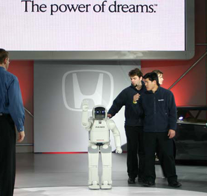 A photo of a small robot getting patted on the back by two men.